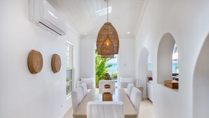 A dining area with a long table, white walls, and a view of the ocean.
