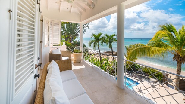 A balcony with a white ceiling fan, a cushioned seating area, and a view of the ocean.