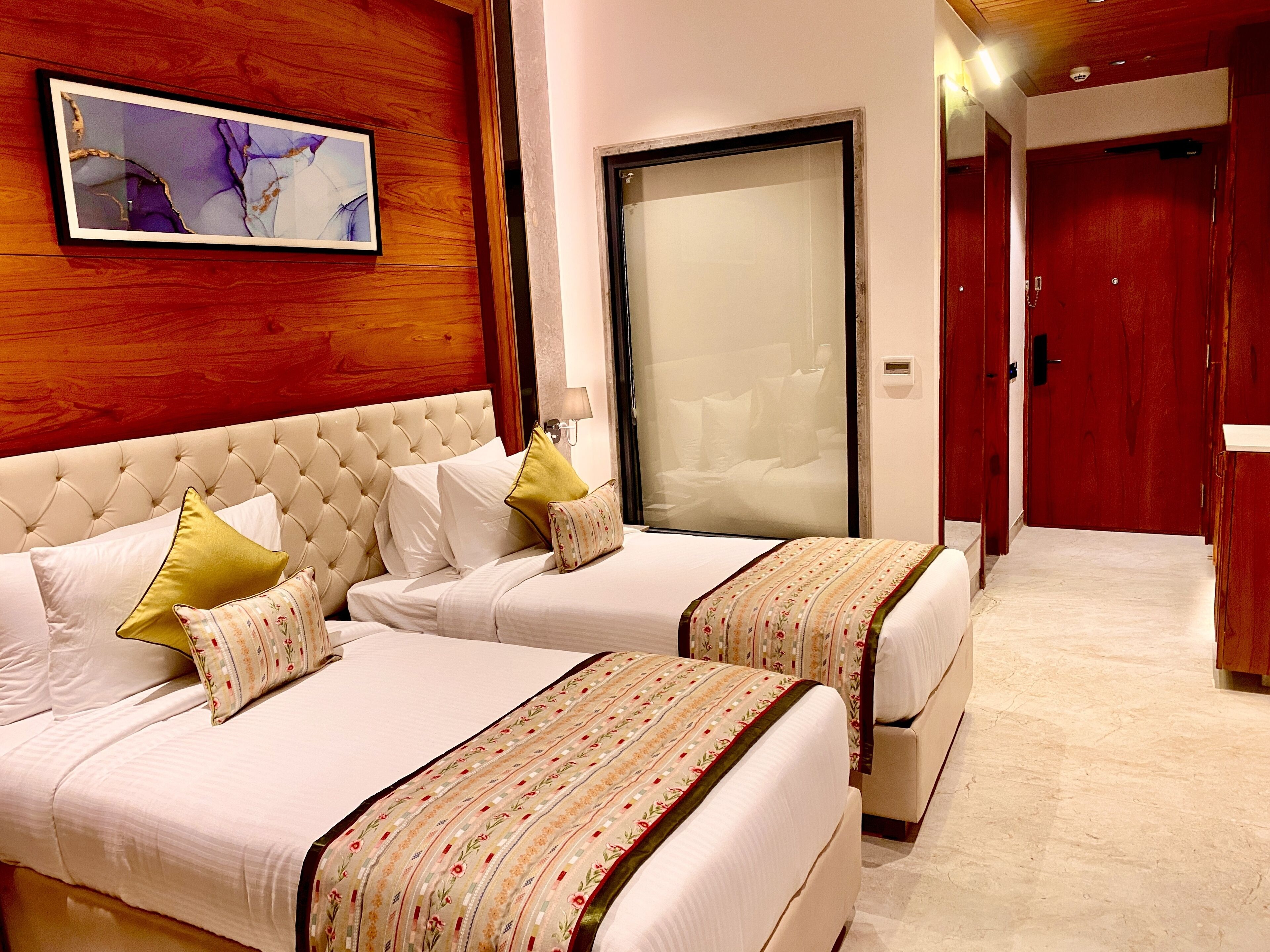 A hotel room with two beds, a large window, a wooden headboard, and a framed artwork on the wall.