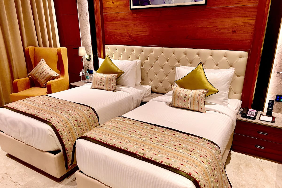 A hotel room with two beds, a chair, a nightstand, and a mirror.