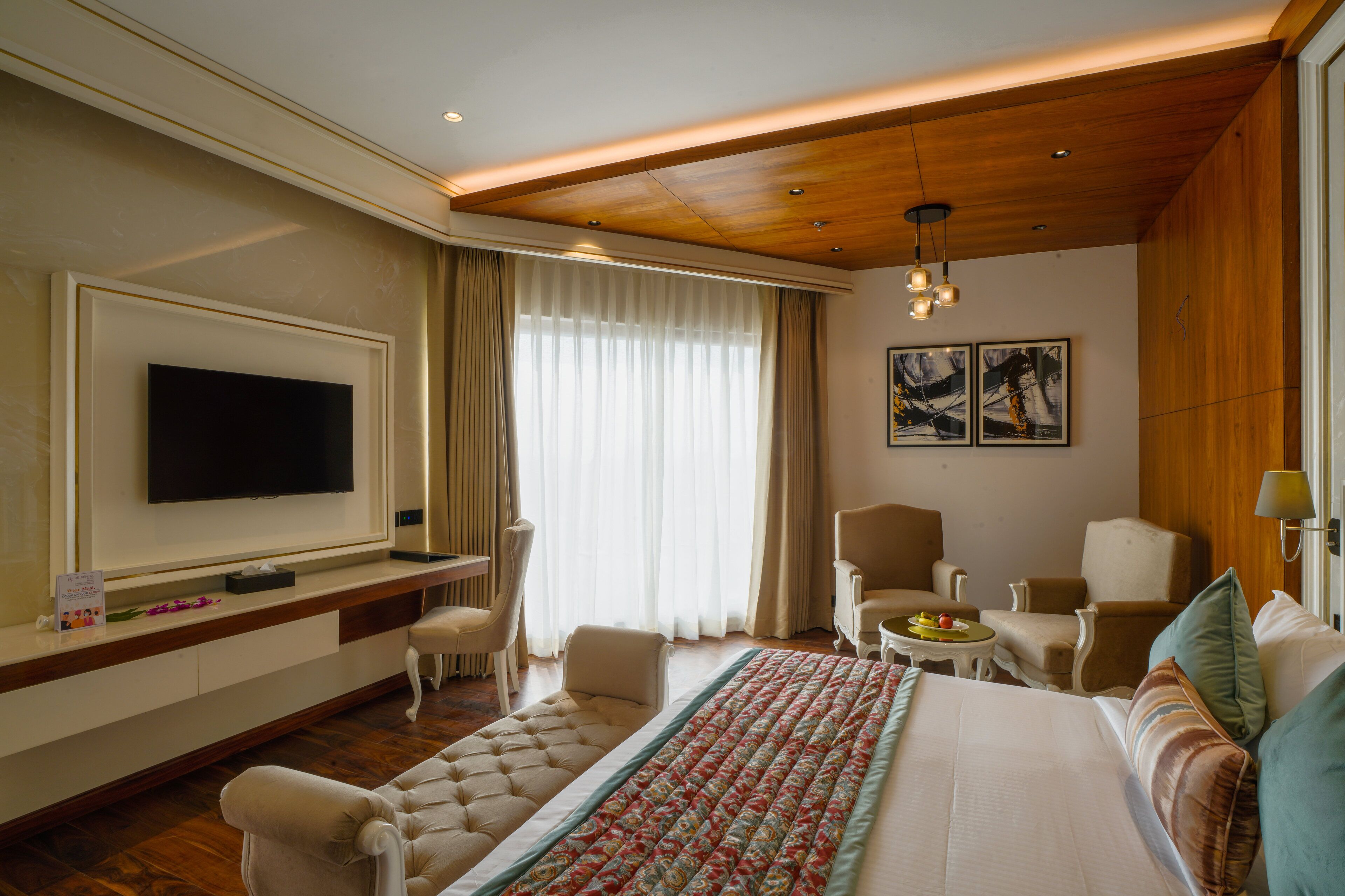 A hotel room with a large bed, a flat-screen TV, a wooden ceiling, and a window with curtains.