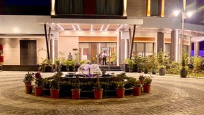 Entrada de hotel con un espacio exterior cubierto, plantas en macetas y una estatua.