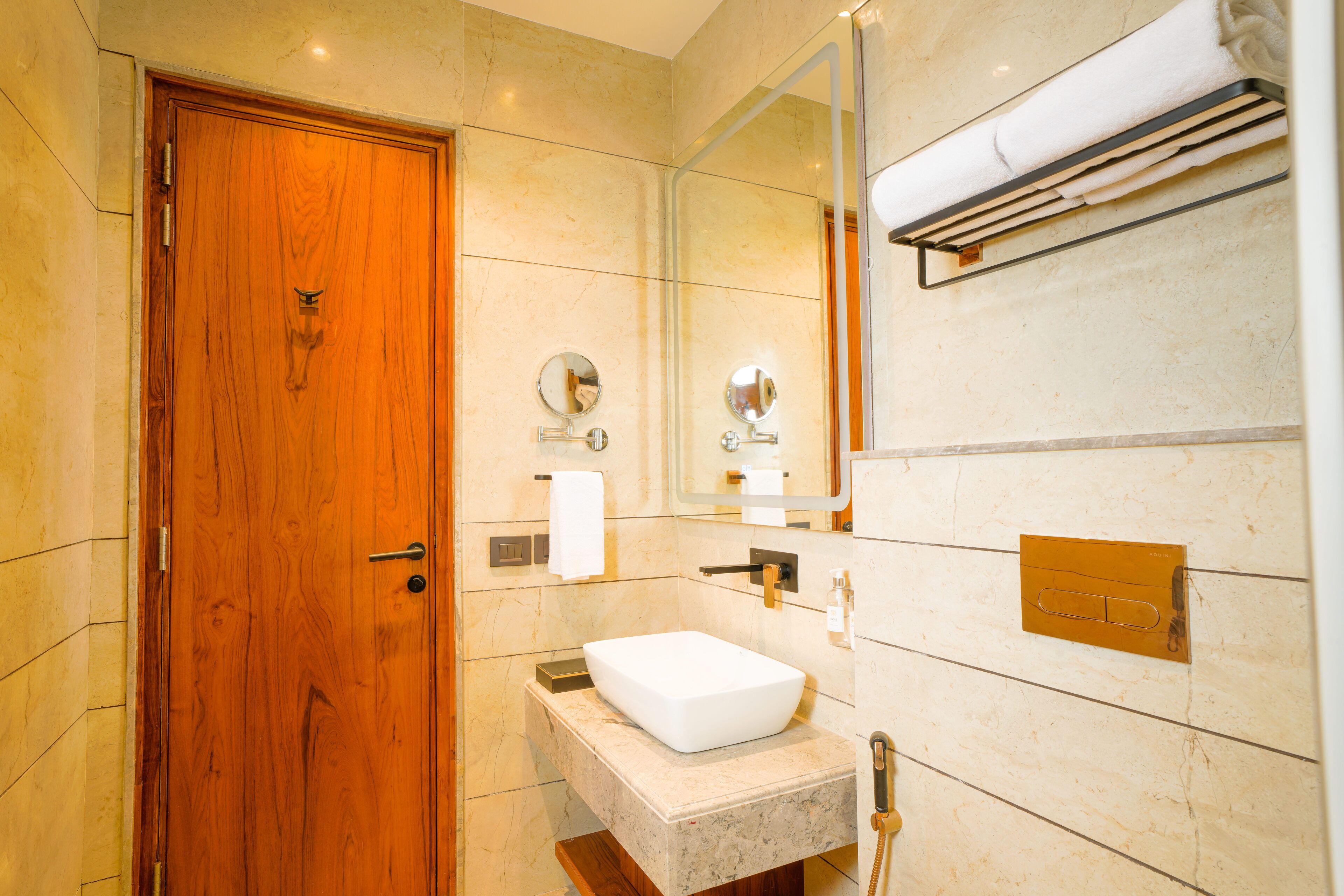 Une salle de bain moderne avec une porte en bois, un lavabo blanc, un miroir et un porte-serviettes.