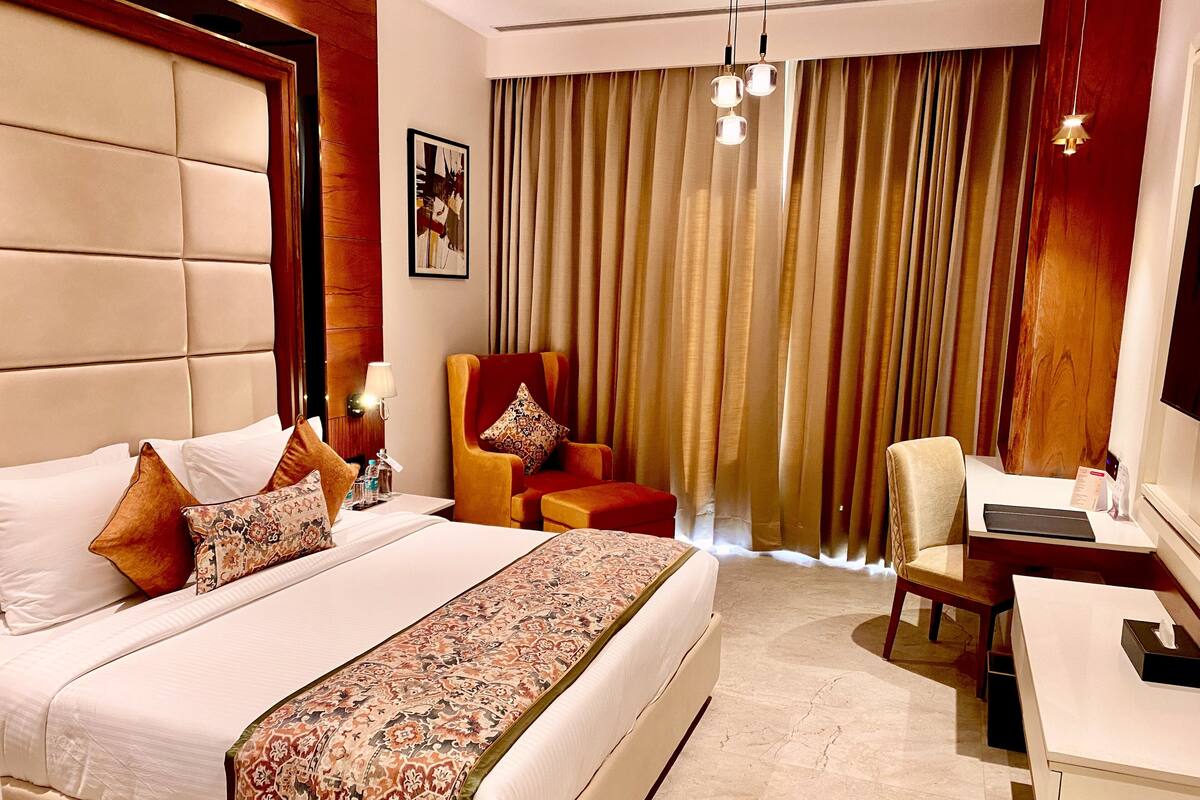 A hotel room with a large bed, a desk, a chair, and a view of the outdoors through curtains.