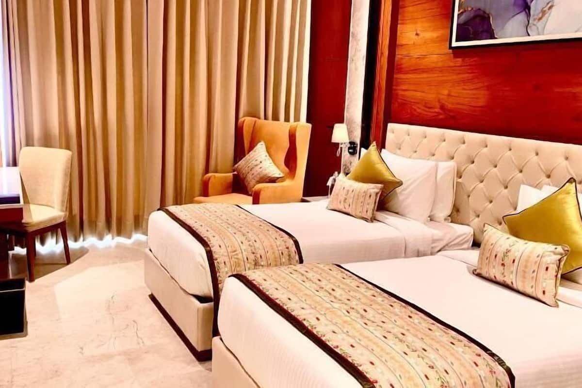A hotel room with two beds, a desk, a chair, and a TV.