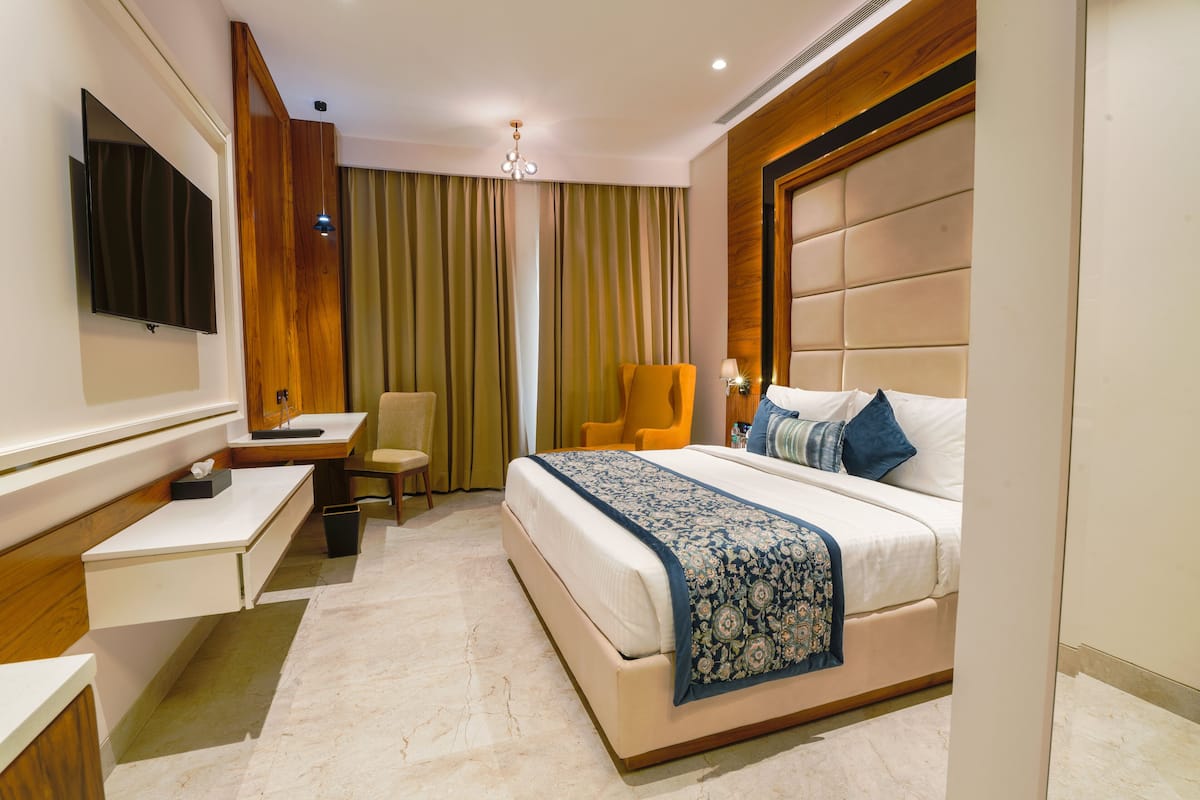 A hotel room with a bed, a desk, a chair, a TV, and a large window with curtains.