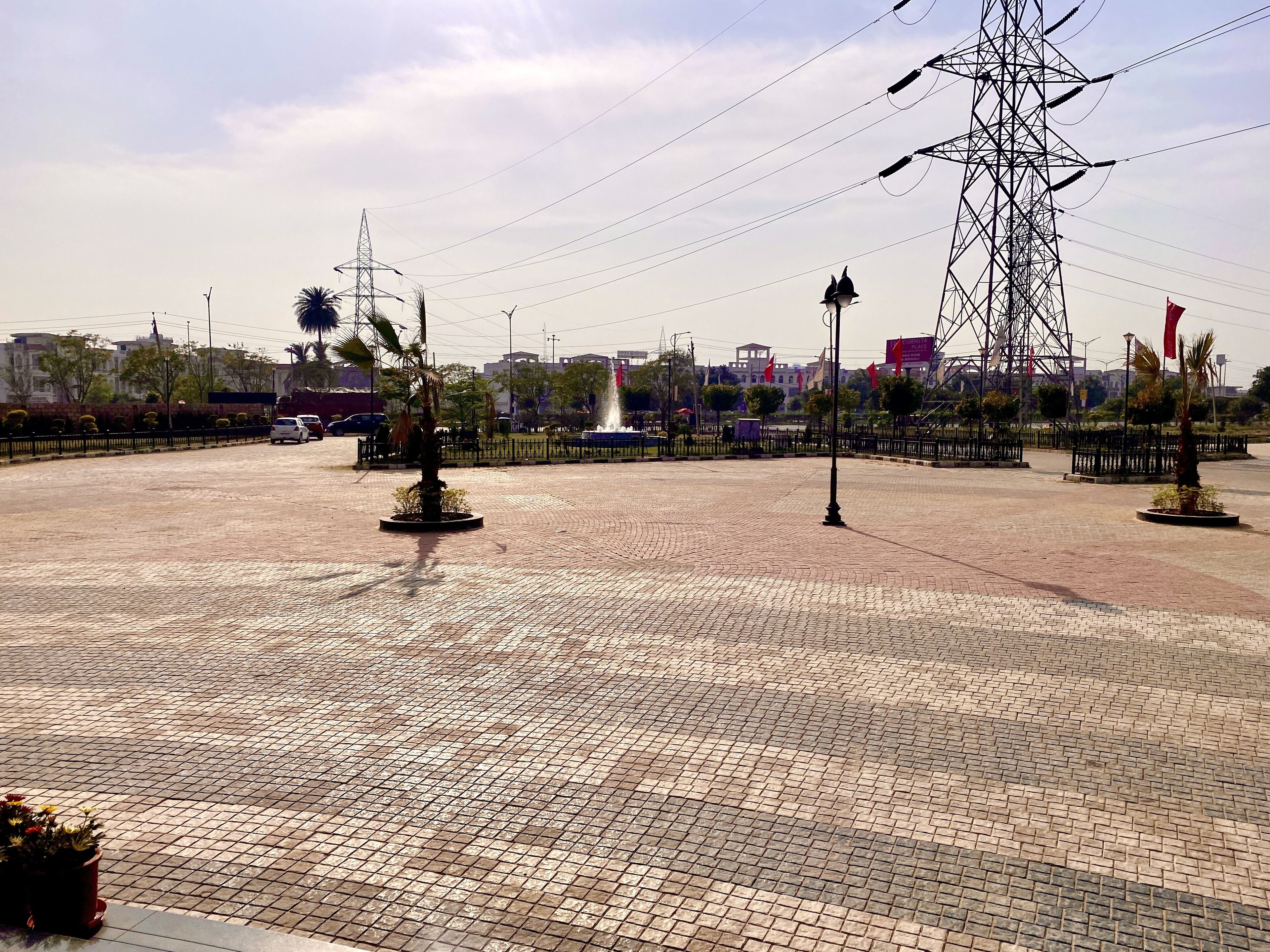 Una plaza pavimentada con una fuente, palmeras y una torre de líneas eléctricas.