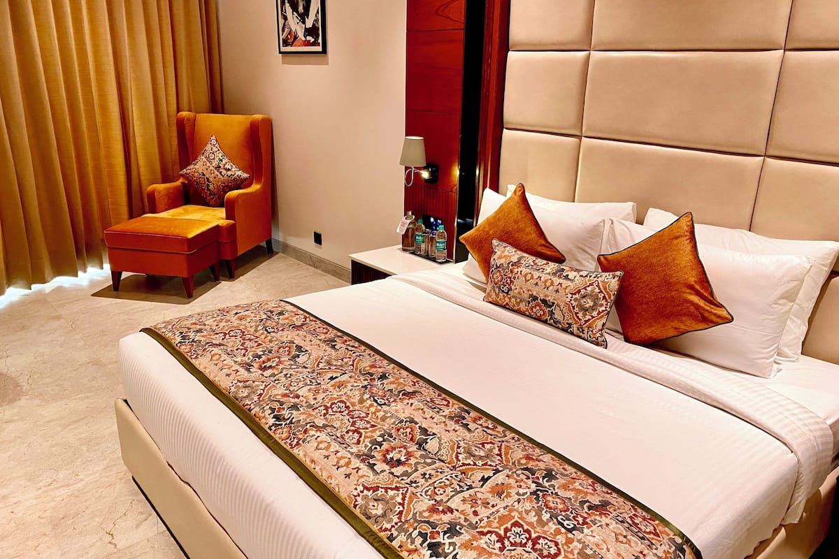 A hotel room with a large bed, a sofa, a nightstand, and a window with curtains.