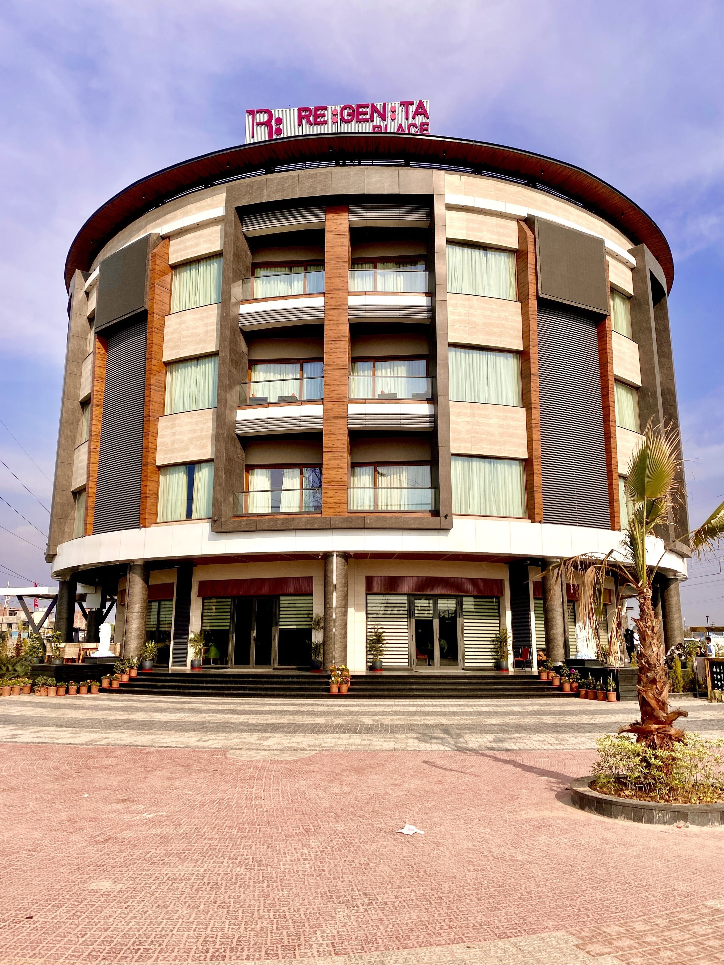 A multi-story hotel with a curved facade, balconies, and a sign reading "RE:GEN:TA".