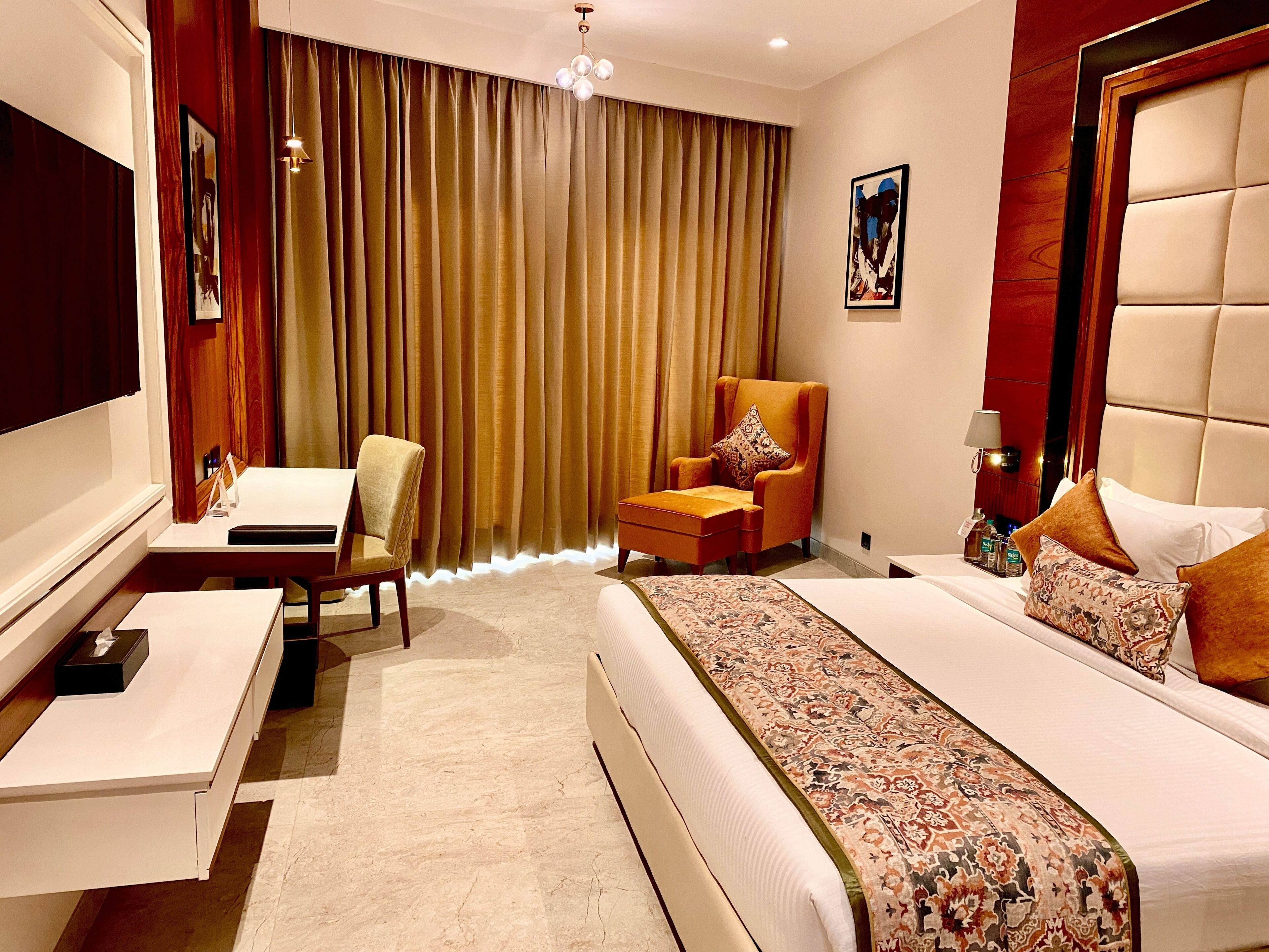 Una habitación de hotel con una cama, un escritorio, una silla y un ventanal con cortinas.