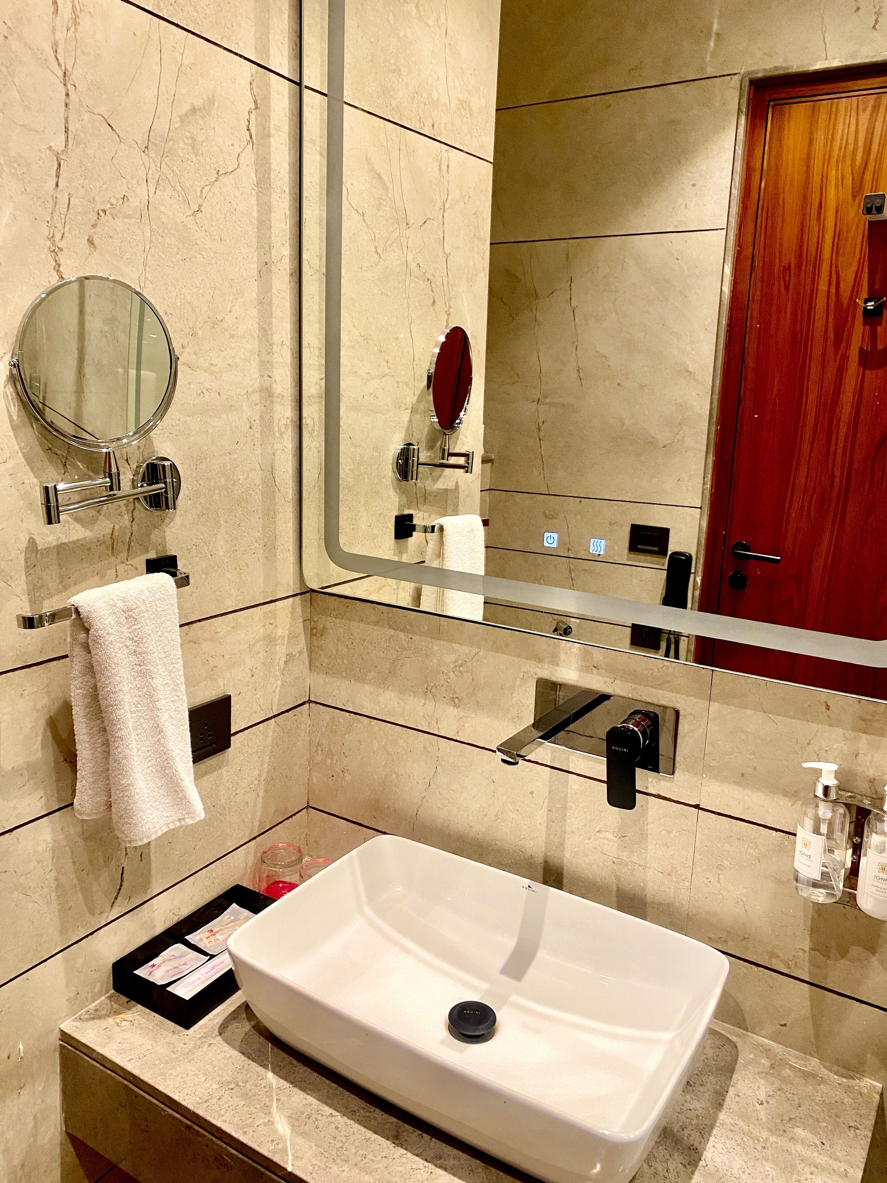 A bathroom with a white sink, a round mirror, a red vanity mirror, and a wooden door.