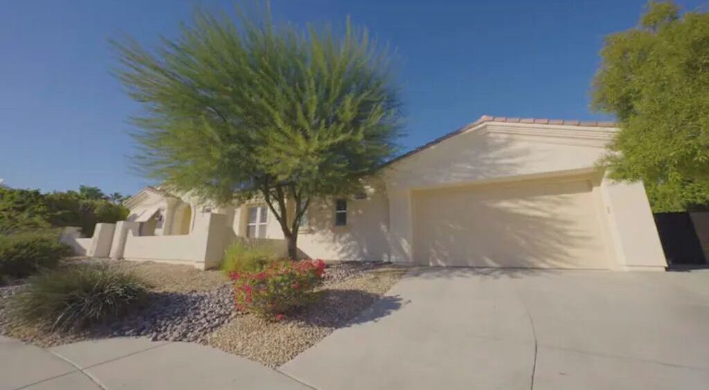 A single-story house with a garage, a small tree, and a gravel driveway.