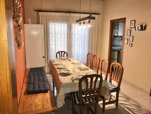 A dining area with a long table set for four, wooden chairs, a cushioned bench, and a refrigerator. - Villa 30 m from Cambrils Beach with Sea Views, Wi-Fi, Terraces and Garden (Cambrils)
