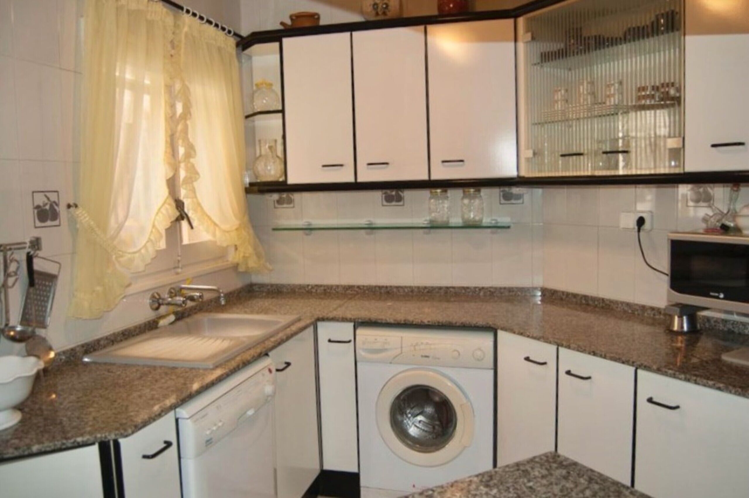 A compact kitchen with a washing machine, a sink, and cabinets.