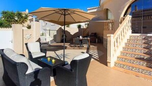 Un patio al aire libre con mobiliario de mimbre, una mesa con bebidas y un gran paraguas.