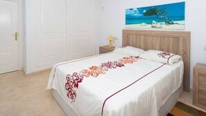 Un dormitorio con una cama, una mesita de noche, un cuadro de una playa y una puerta cerrada.