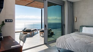 Una moderna camera d'hotel con un'ampia porta scorrevole in vetro che dà su un balcone con vista sul mare.