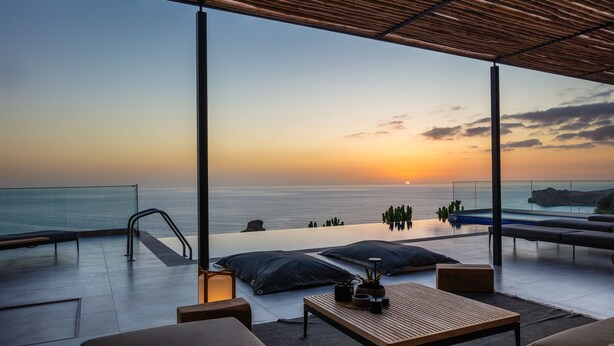 Una terrazza sul tetto con vista sul tramonto sul mare, una piscina a sfioro e area salotto all'aperto.