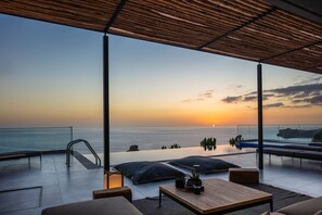 A rooftop terrace with a view of the sunset over the sea, an infinity pool, and outdoor seating.