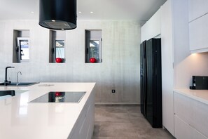 A modern kitchen with a central island, black appliances, and a view through windows.