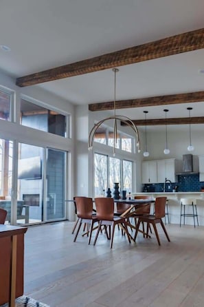 A spacious dining area with a wooden ceiling, large windows, and modern pendant lighting.