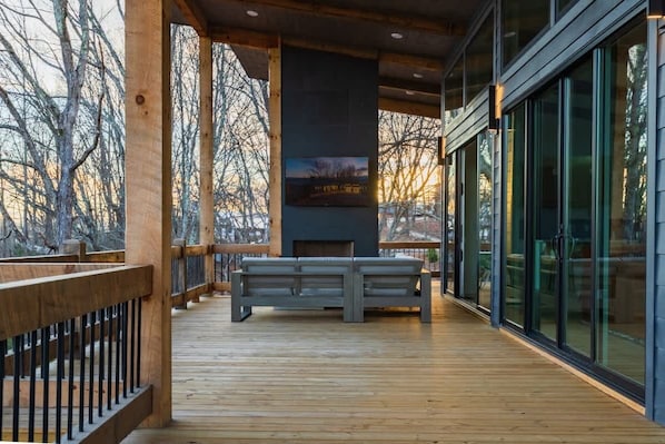 A wooden deck with a bench, a fireplace, and large windows.