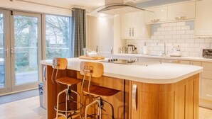 A modern kitchen with a large island, bar stools, and a view through the glass doors. - Carnanamish a Luxurious Cottage in Tobermory (Tobermory)