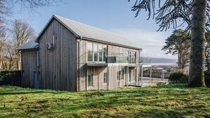 A modern wooden building with a large glass extension, a covered outdoor seating area, and a view of the sea. - Carnanamish a Luxurious Cottage in Tobermory (Tobermory)