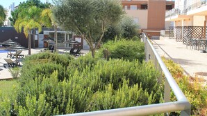 A balcony with a metal railing, a palm tree, and a building with a tiled roof in the background. - Cabanas Gardens,  4px, pool view (Cabanas de tavira)