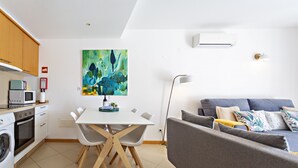 A modern kitchen with white cabinets, a dining table with chairs, a gray sofa, and a painting on the wall. - Cabanas Gardens, 4px, pool viewr (Cabanas de tavira)