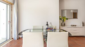 A dining area with a glass table, white chairs, a white cabinet, and a mirror on the wall.