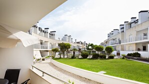 A balcony with a view of a courtyard, a dining area with chairs, and a white building with multiple balconies. - Cozy apartment, access to swimming pool, barbecue (Tavira)
