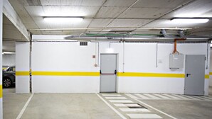 A parking garage with white walls, yellow stripes, and a closed door. - Cozy apartment, access to swimming pool, barbecue (Tavira)