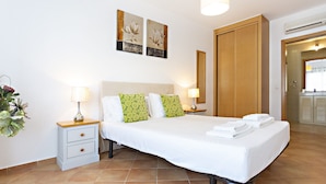 A hotel room with a bed, two bedside tables with lamps, a potted plant, and artwork on the wall. - Cozy apartment, access to swimming pool, barbecue (Tavira)