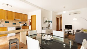 A modern kitchen with wooden cabinets, a glass dining table, and a built-in oven. - Cozy apartment, access to swimming pool, barbecue (Tavira)