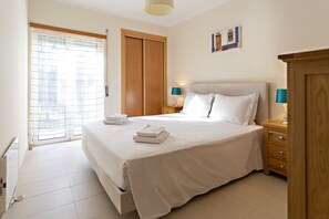 Una habitación de hotel con una cama, un armario de madera, una mesita de noche con lámparas y una puerta con ventanal.
