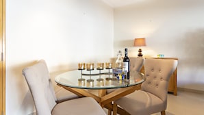 Una mesa redonda de vidrio con seis candelabros, una botella y una lámpara sobre un suelo de madera.