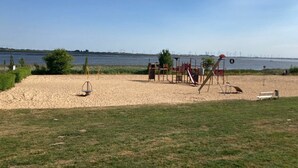 A playground with swings and slides near a body of water, with wind turbines in the background. - Vacation apartment "Norderhus" (WH2) with 70sqm - quiet central location - with balcony (Tönning)