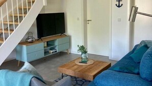 A modern living room with a staircase, a blue sofa, a coffee table, and a TV. - Vacation apartment "Norderhus" (WH2) with 70sqm - quiet central location - with balcony (Tönning)