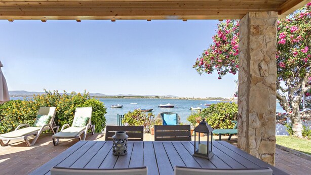 A covered outdoor seating area with a table and chairs, overlooking a body of water with boats. - Beach house, 2 steps from the ocean! (Faro)
