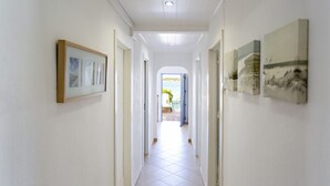 A hallway with white walls, tiled floor, framed pictures, and doors leading to other areas. - Beach house, 2 steps from the ocean! (Faro)