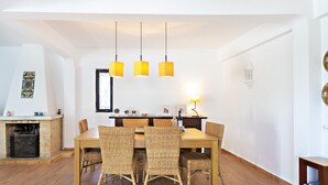 A dining area with a wooden table and wicker chairs, a fireplace, and hanging pendant lights.