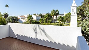 A rooftop terrace with a white wall, a small white tower, and palm trees.