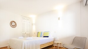A bedroom with a bed, bedside table, chair, and a wall-mounted light fixture.