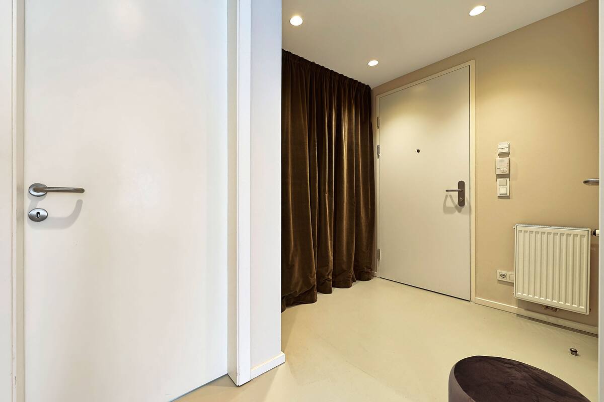 A hotel room with a white door, a radiator, and a brown curtain.