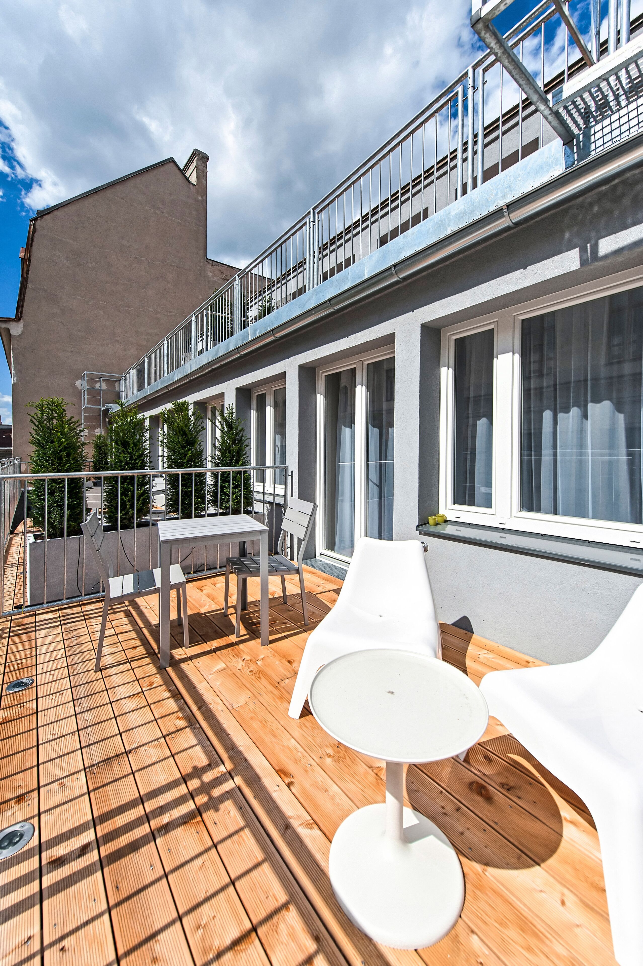 Una terraza en la azotea con piso de madera, sillas de lounge blancas, una mesita y barandilla.
