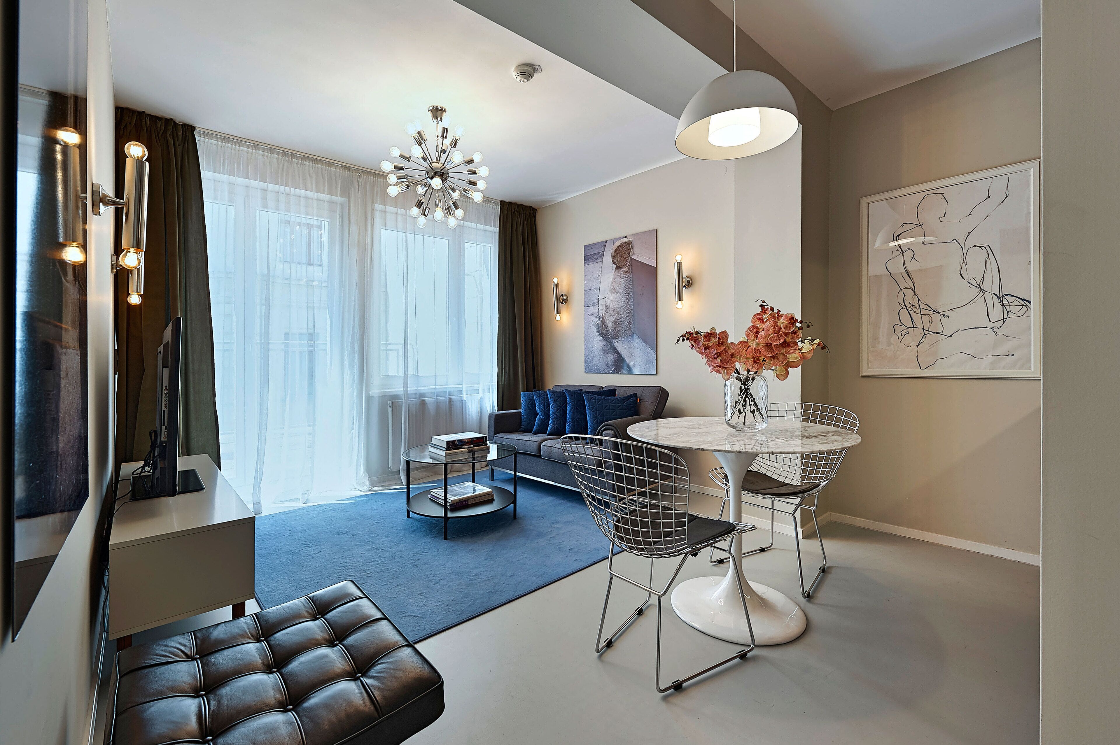A modern living room with a sofa, a dining table with chairs, a TV, and a chandelier.