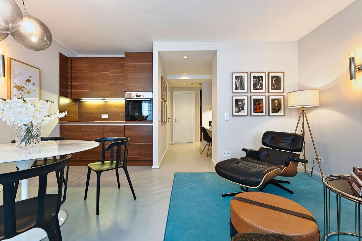 A modern living room with a dining area, a kitchen with wooden cabinets, and a staircase leading to another level.