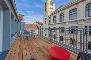 A wooden deck with a red table and chairs, overlooking a historic building with a clock tower.