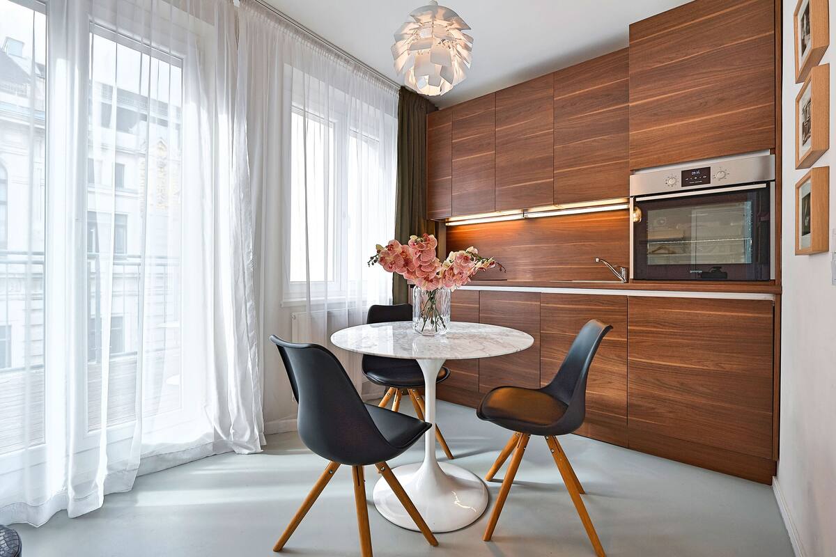 A modern kitchen with wooden cabinets, a built-in oven, and a round dining table with chairs.